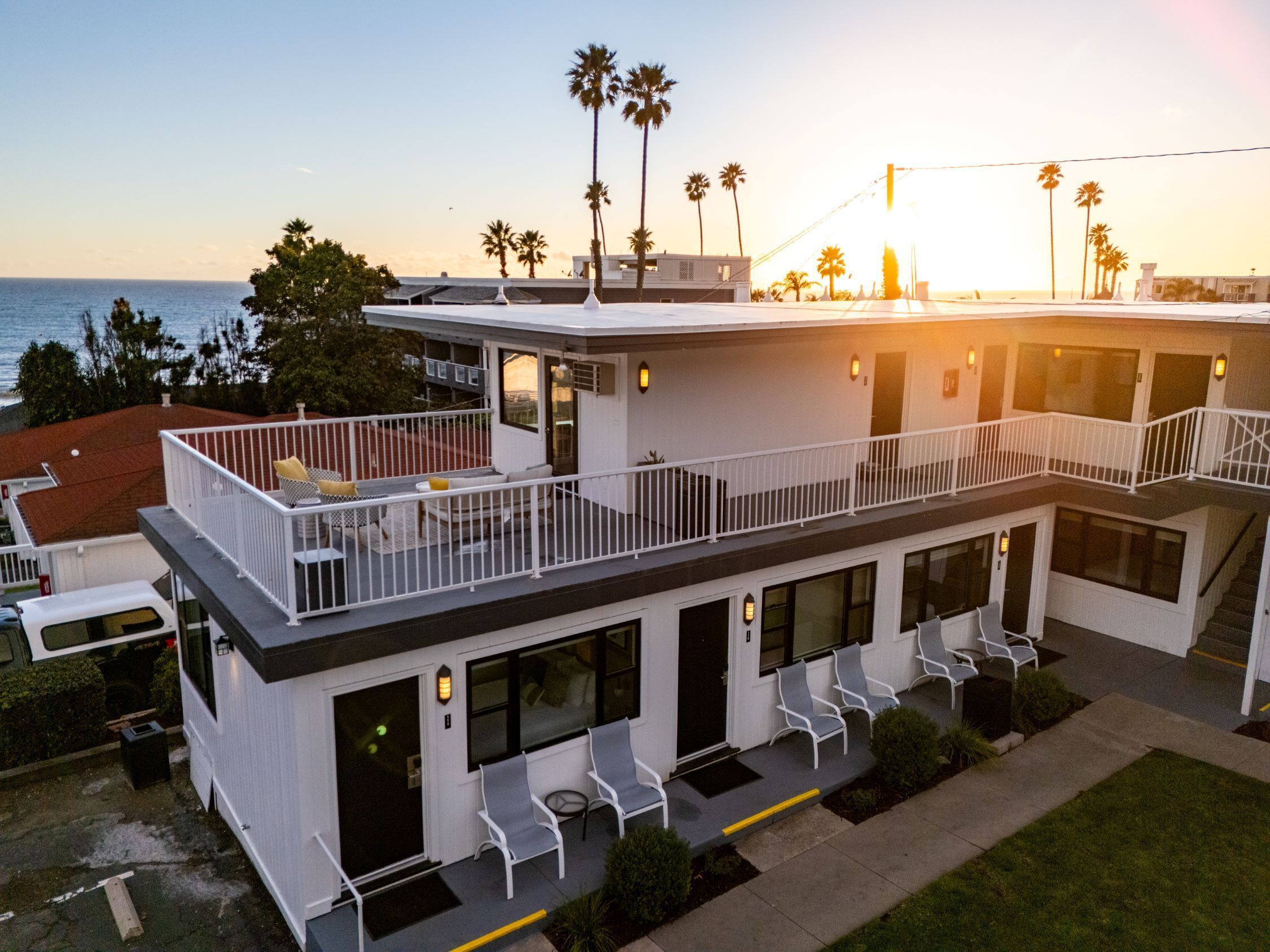 A modern two-story building with a balcony, large windows, and a view of the ocean.