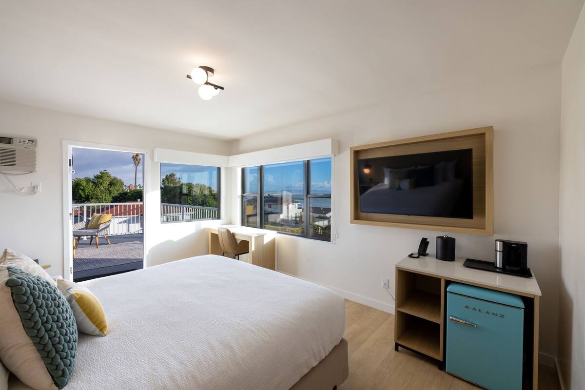 A modern hotel room with a large bed, a desk, and a view of the city.