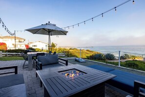 An outdoor patio with a fire pit, seating, and string lights. - The Tides Oceanview Inn and Cottages (Pismo Beach)