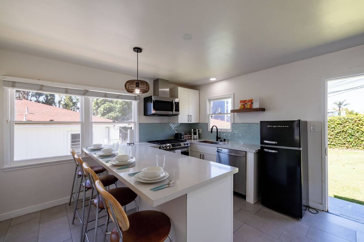 A modern kitchen with white cabinetry, a central island, bar stools, a black refrigerator, and a view of the outdoors.