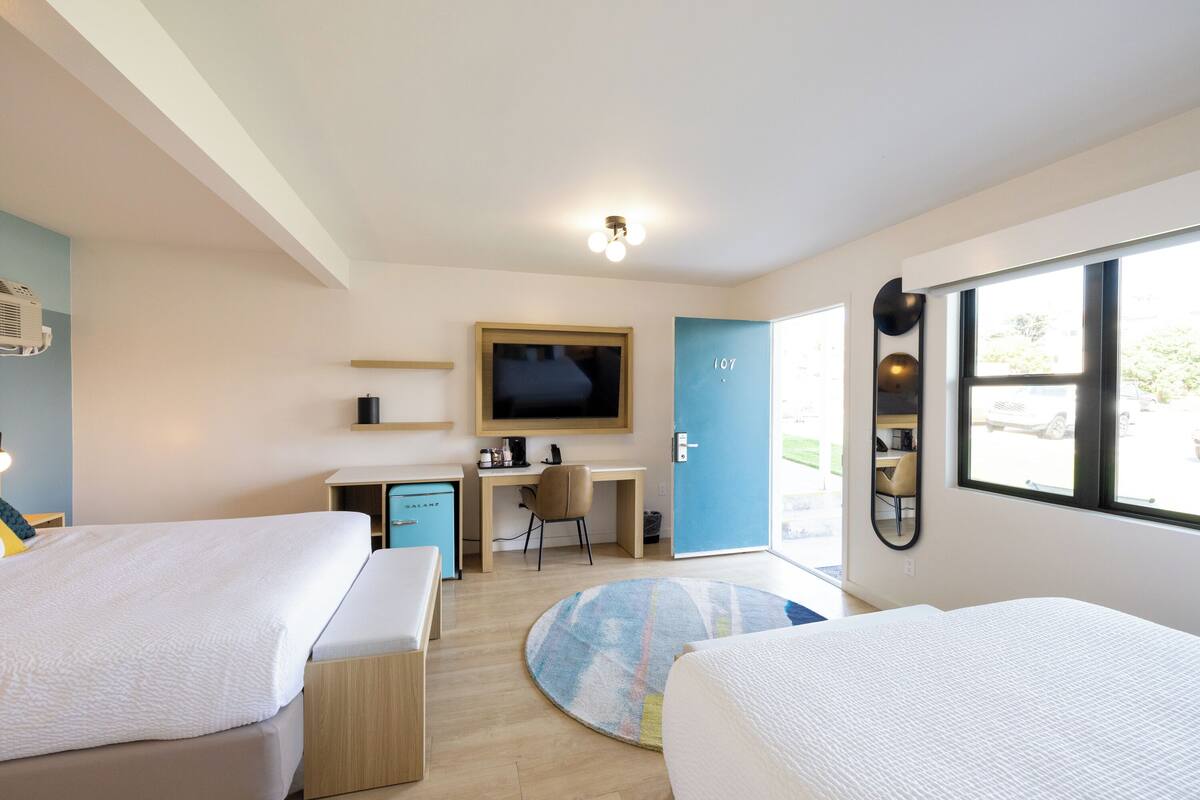A modern hotel room with two beds, a desk, a television, and a large window.