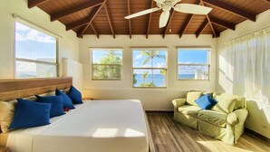 Un dormitorio con cama, sofá verde y grandes ventanas con vista al mar.