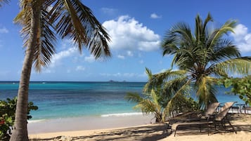 Di pantai, pasir putih, kursi berjemur, dan payung pantai