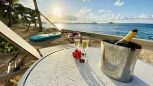 Una mesa en la playa con una botella de champán, dos copas y un adorno rojo.