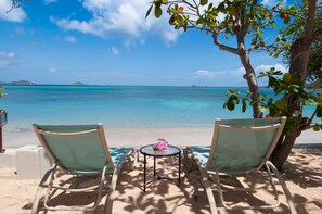 Two beach chairs facing a sandy beach with a clear view of the ocean and distant islands.
