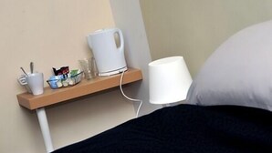 Une chambre d’hôtel équipée d’une table de chevet sur laquelle se trouvent une bouilloire, une tasse et un verre.