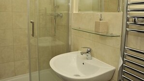 Une salle de bain avec une douche à parois de verre, un lavabo blanc et une étagère en verre au-dessus du lavabo.