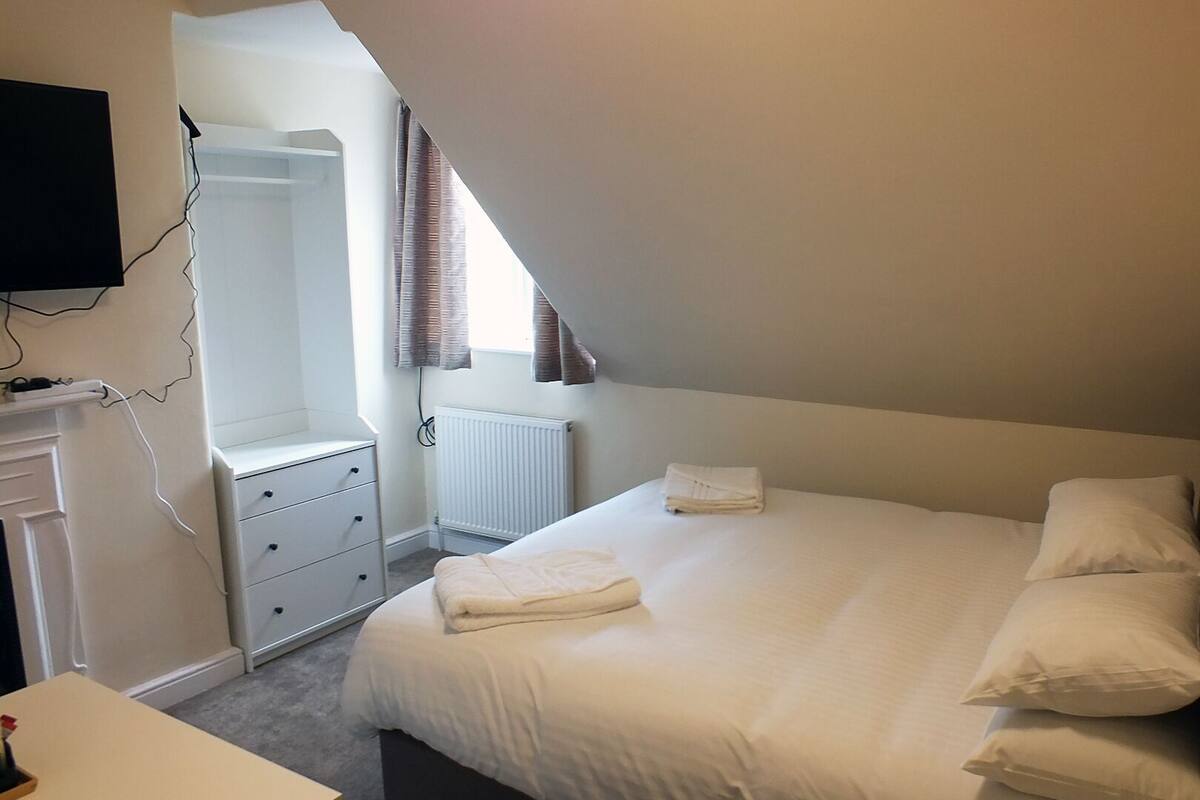 A bedroom with a bed, a dresser, a radiator, and a TV mounted on the wall.