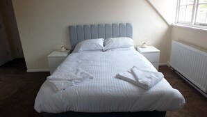 Una cama bien hecha con sábanas y toallas blancas, un cabecero tapizado en azul y mesitas de noche blancas con lámparas.