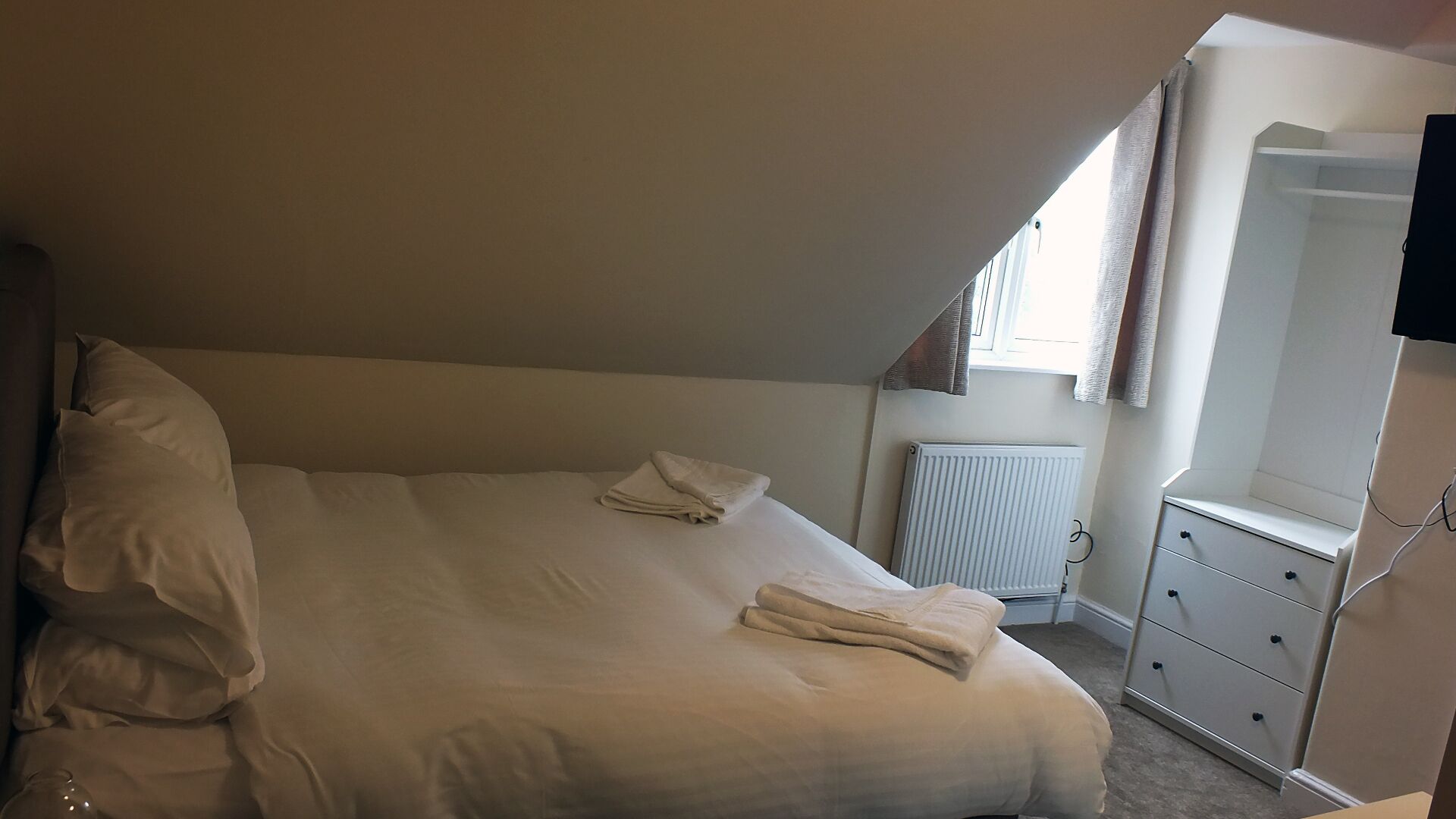 Een slaapkamer met een bed, een dressoir, een radiator en een raam met gordijnen.