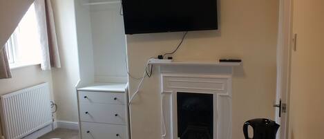 A bedroom with a white wardrobe, a fireplace, a television mounted above the fireplace, and a radiator.