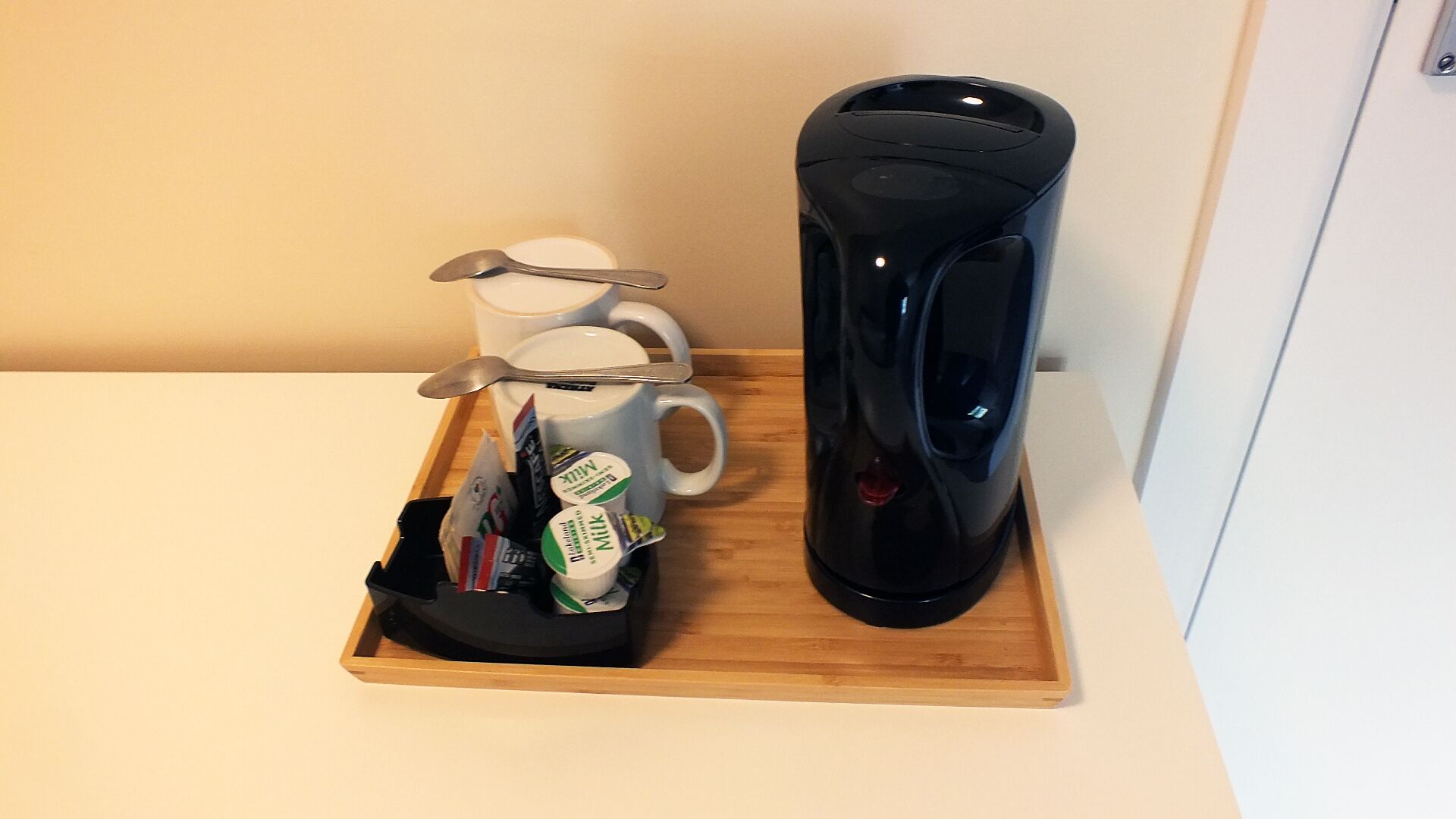 A tray with a coffee maker, two mugs, and a spoon on a wooden surface.
