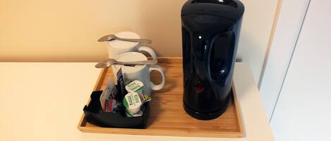 A tray with a coffee maker, two mugs, and a spoon on a wooden surface.