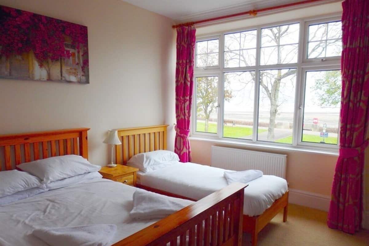 A room with two wooden beds, a nightstand, a window with curtains, and a painting on the wall.