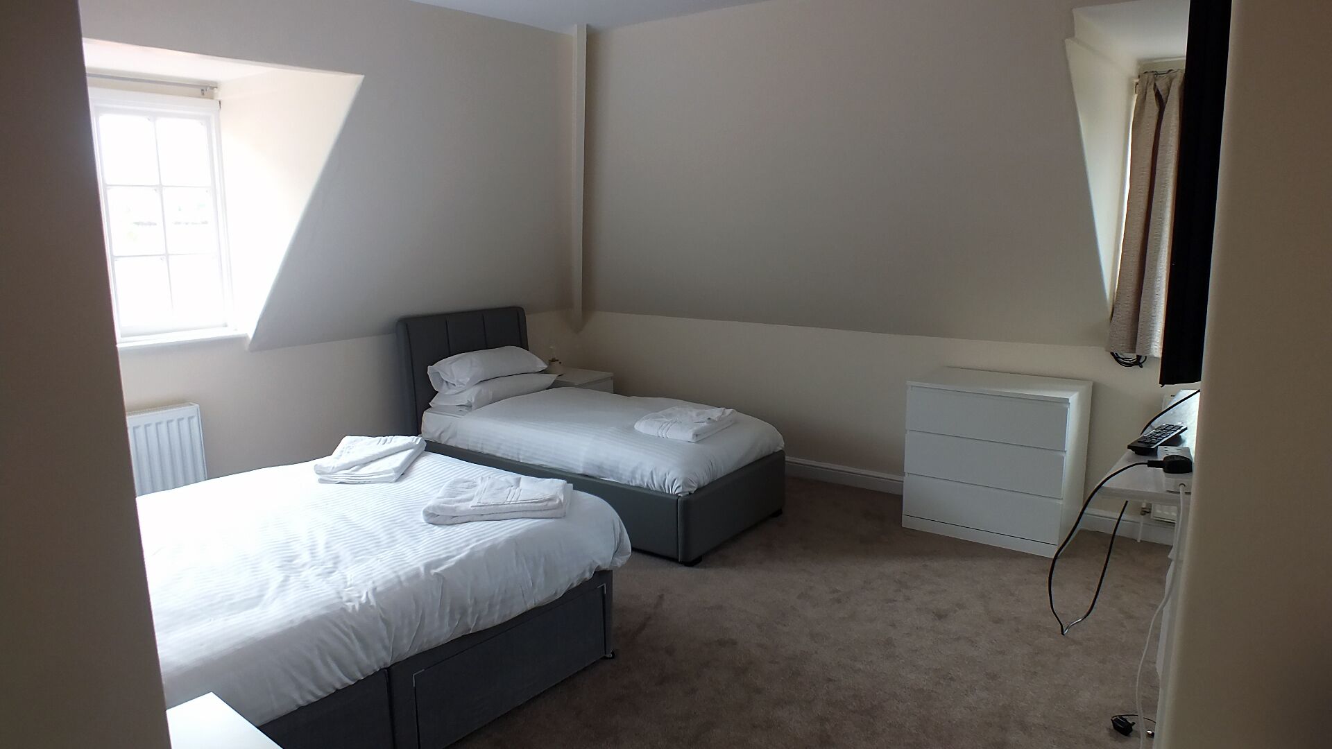 Un dormitorio con dos camas, una mesita de noche, un aparador y una ventana.