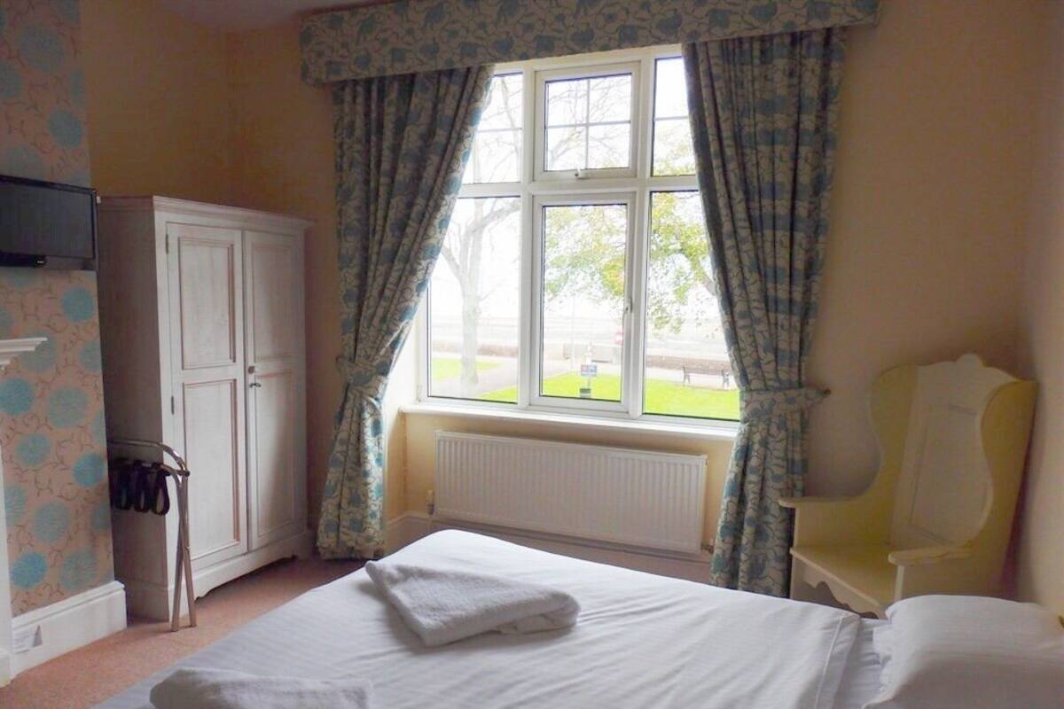 A bedroom with a bed, a window with curtains, a radiator, and a wardrobe.