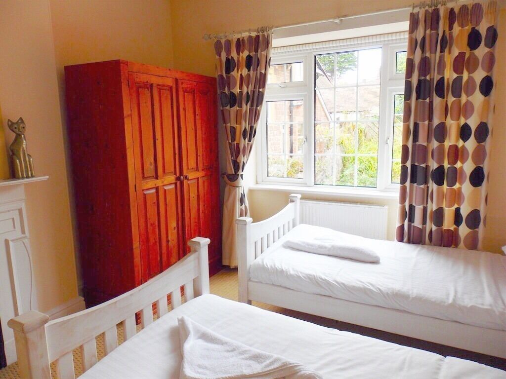 Un dormitorio con dos camas individuales, un armario de madera y una ventana con cortinas.