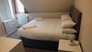 A neatly made bed with white linens, a bedside lamp, and a small bedside table.