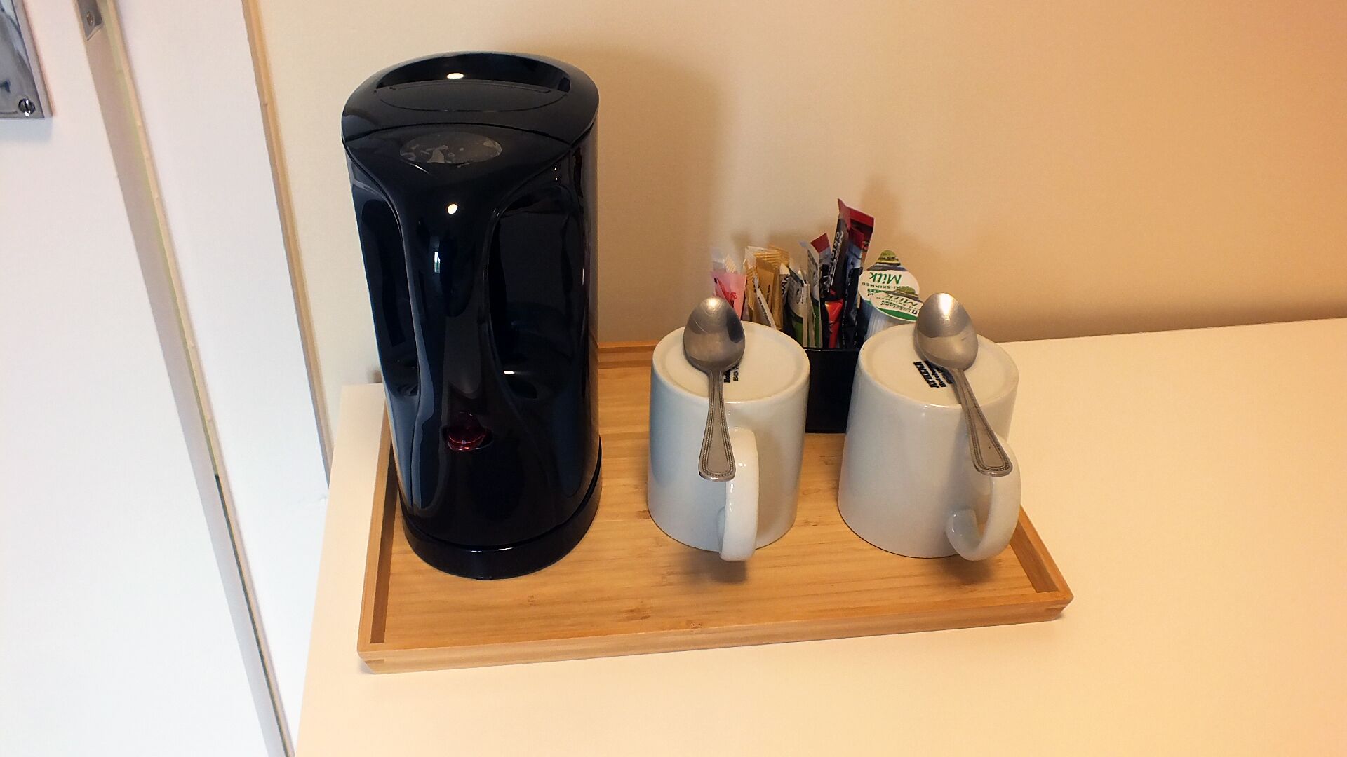 A coffee maker, two mugs with spoons, and a tray on a countertop.