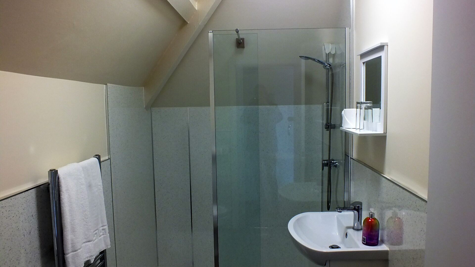 A modern bathroom with a glass-enclosed shower, a white sink with toiletries, and a towel hanging on a rack.
