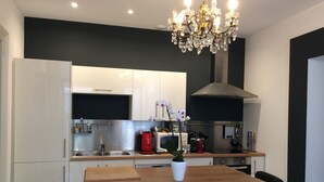 Une cuisine moderne avec des meubles blancs, un plan de travail en bois, une chaise noire et un lustre.