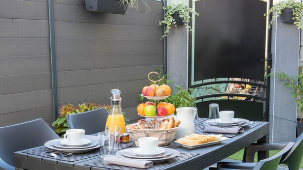 Un espace de restauration en plein air avec une table dressée pour le petit-déjeuner, comprenant des fruits, des viennoiseries et des boissons.