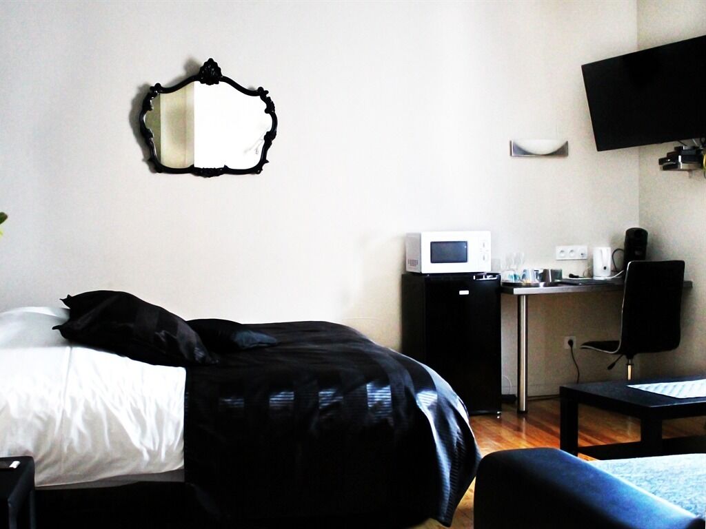 A hotel room with a bed, a desk with a computer, a microwave, a chair, and a flat-screen TV mounted on the wall.