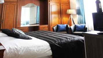 Una habitación de hotel con una cama grande, un escritorio, una silla, una lámpara y un televisor.