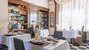 Un espace repas avec des tables préparées pour le petit-déjeuner, agrémenté d’un lustre, de bibliothèques et offrant une vue sur la ville.