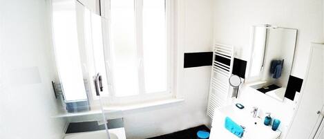 A modern bathroom with a white sink, mirror, and white cabinets. There is a window providing natural light and a blue mat on the floor.