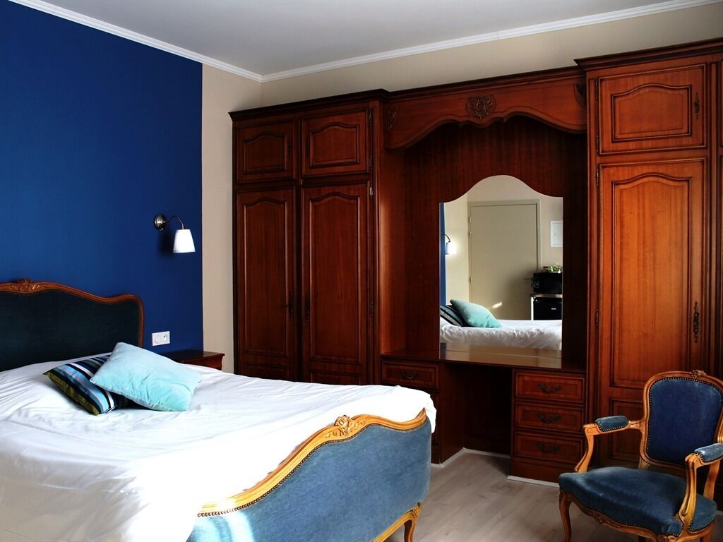 Een slaapkamer met een groot bed, een houten garderobe, een spiegel en een blauwe stoel.