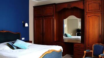 Een slaapkamer met een groot bed, een houten garderobe, een spiegel en een blauwe stoel.