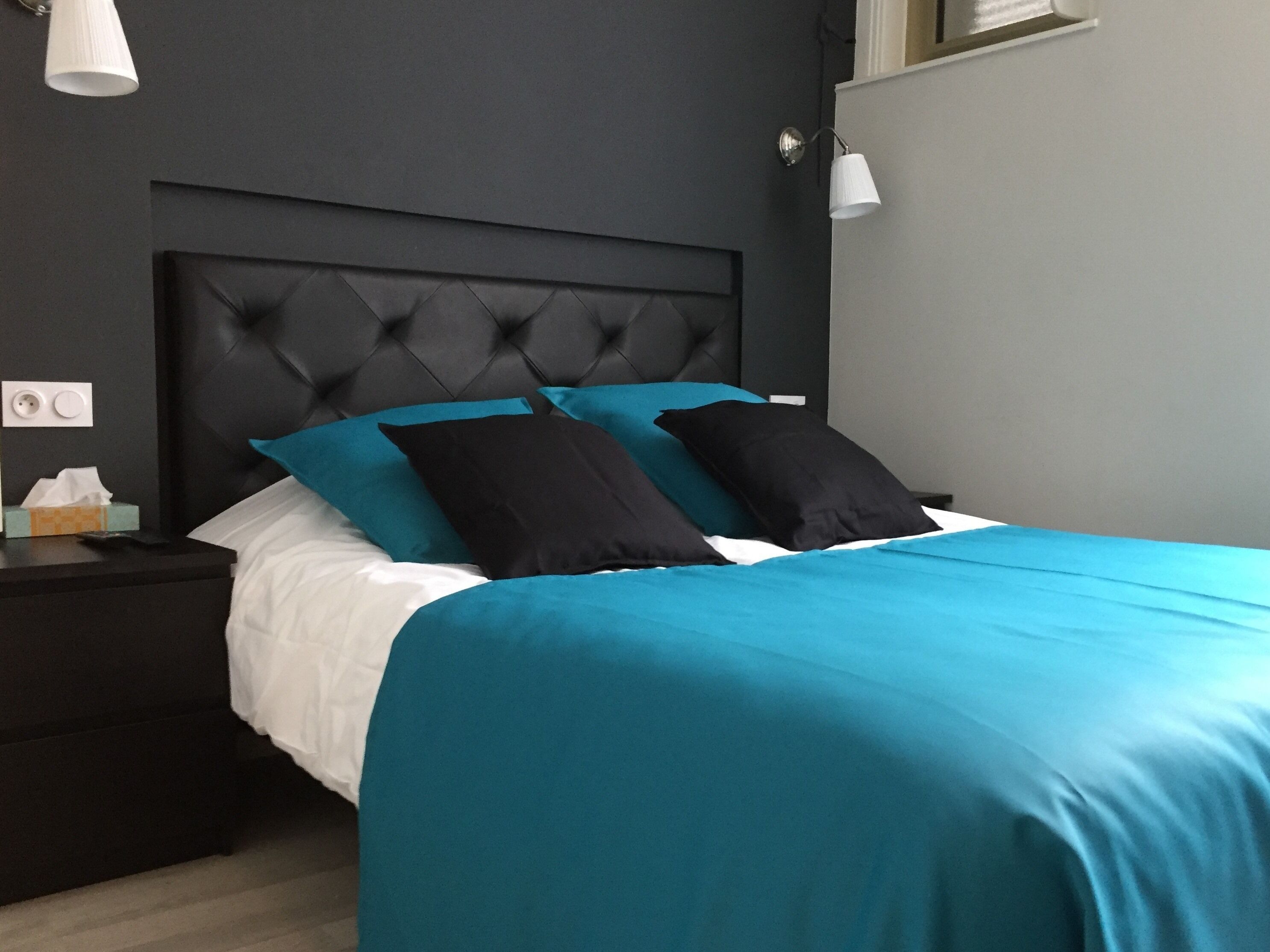 A neatly made bed with a black headboard and teal bedding.