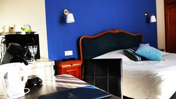 A hotel room with a bed, bedside table, and a desk with a laptop and coffee maker.