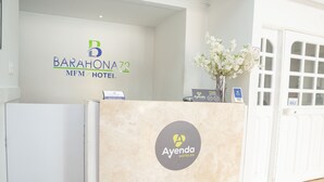 Un mostrador de recepción de hotel con un cartel que dice Barahona 72 MFM Hotel y el logotipo de Ayenda Hotels.