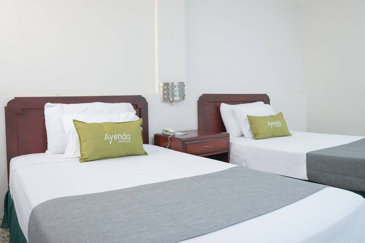 Habitación de hotel con dos camas, cada una con una almohada y una mesita de noche.