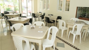 Un comedor con varias mesas y sillas, ventanas amplias con vistas al exterior y un ventilador de techo.