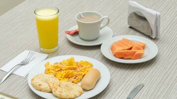 A breakfast setting with a plate of eggs, toast, and a hot dog, a glass of orange juice, a cup of coffee, and a plate of sliced fruit.