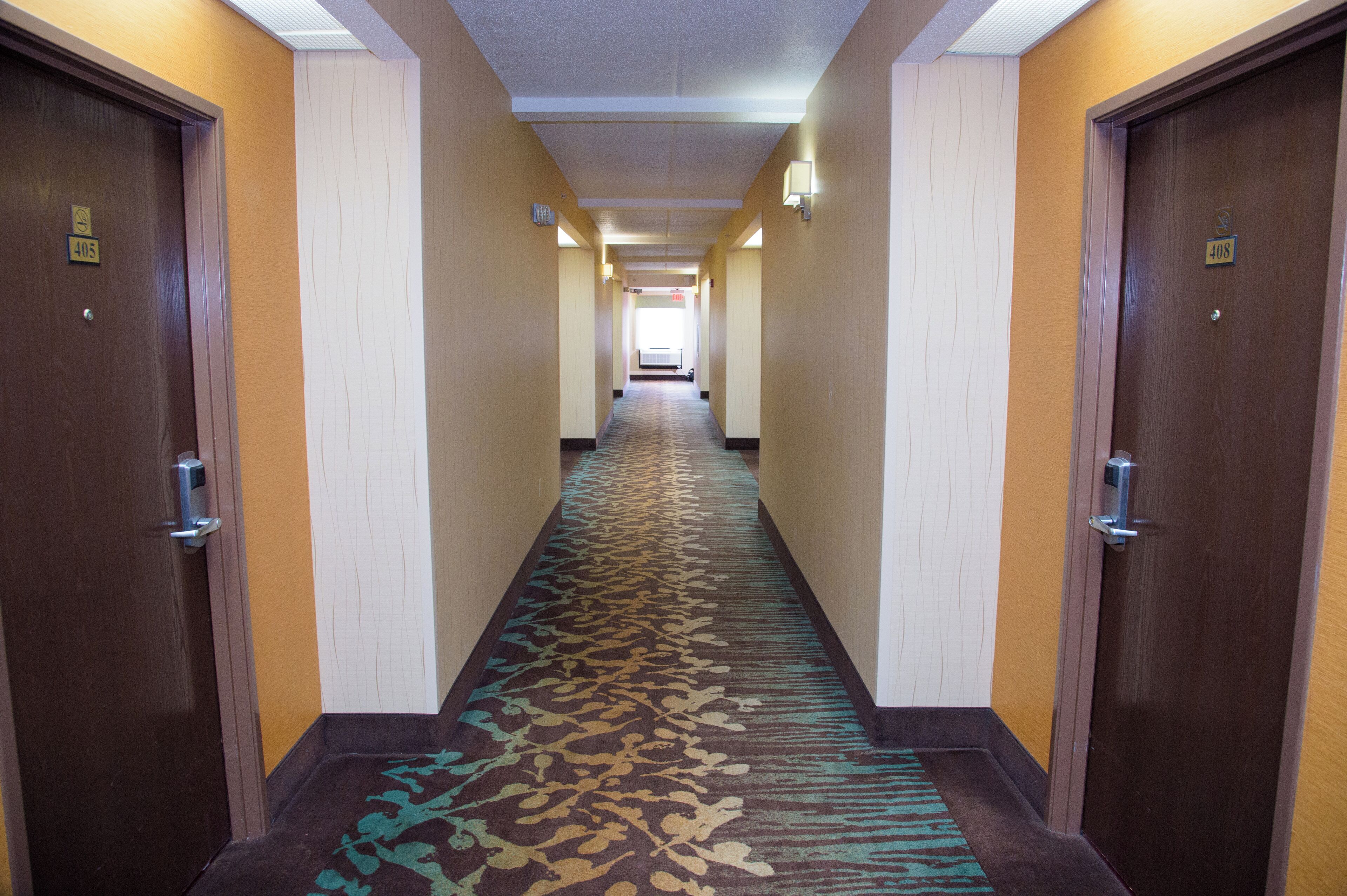 A hotel hallway with carpeted floors, doors on both sides, and a light fixture on the ceiling.