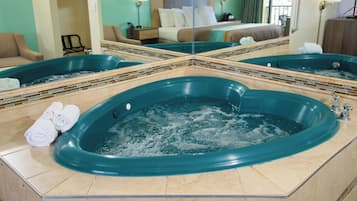 A hotel room with a large bathtub, a bed, a mirror, and a seating area.