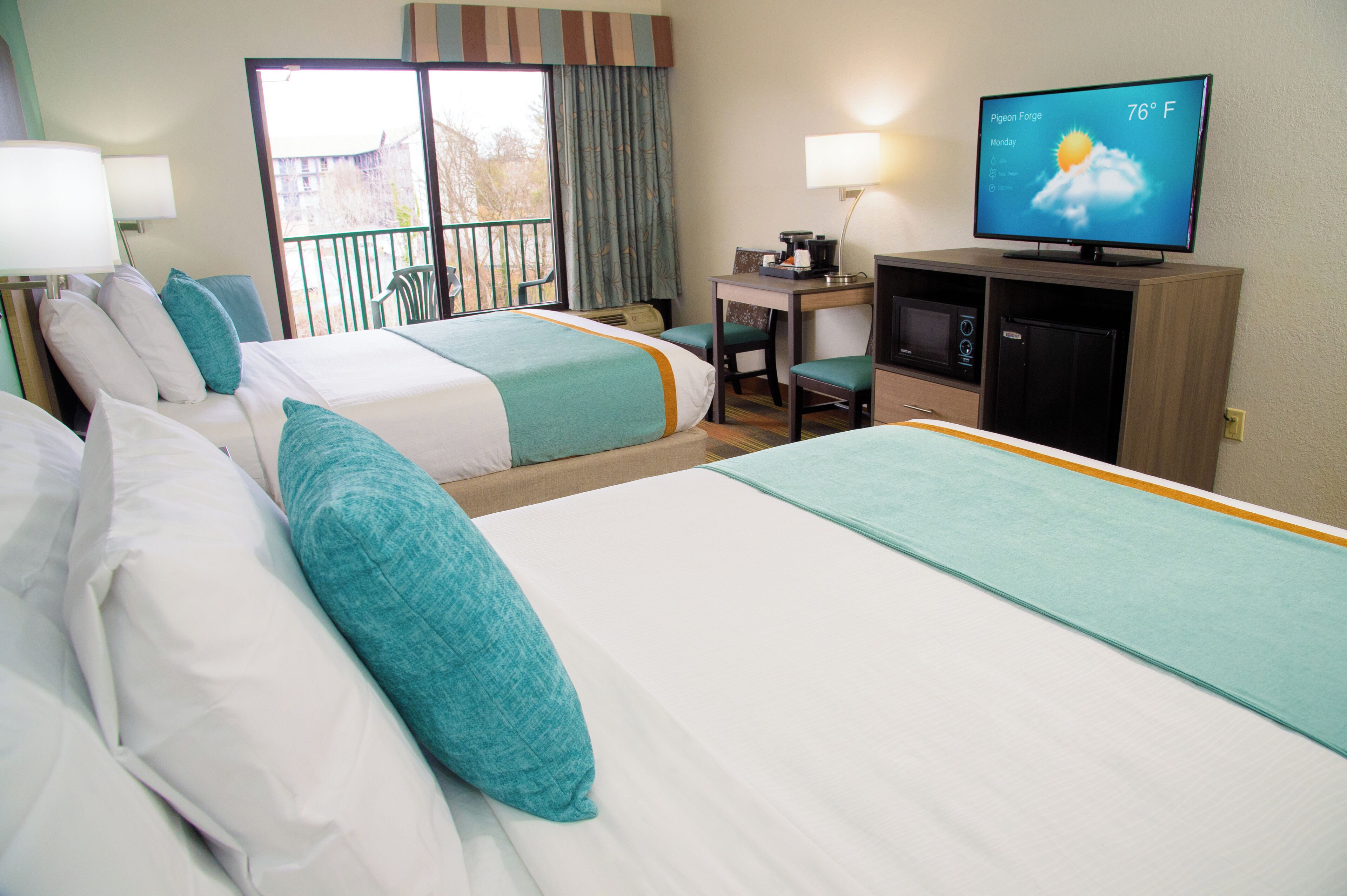 A hotel room with two beds, a desk, a television, and a balcony.