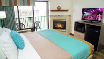 A hotel room with a bed, a television, a fireplace, and a balcony with chairs.
