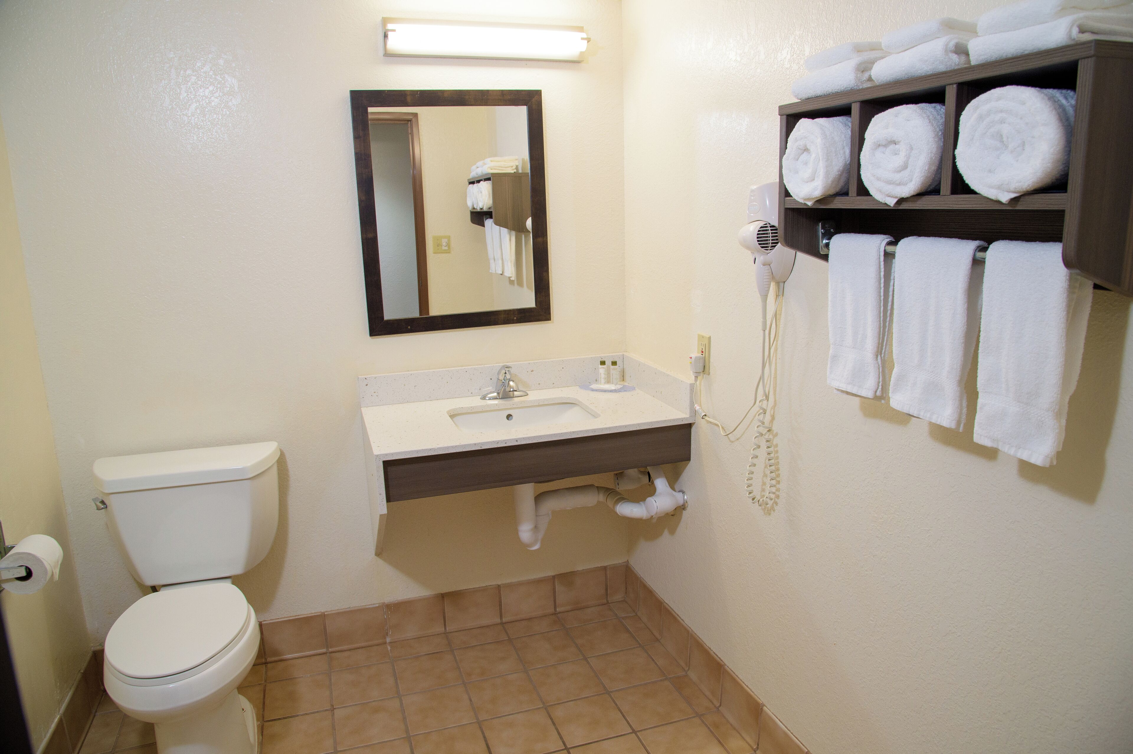 Un baño con inodoro, lavamanos, espejo, toallero y secador de pelo.