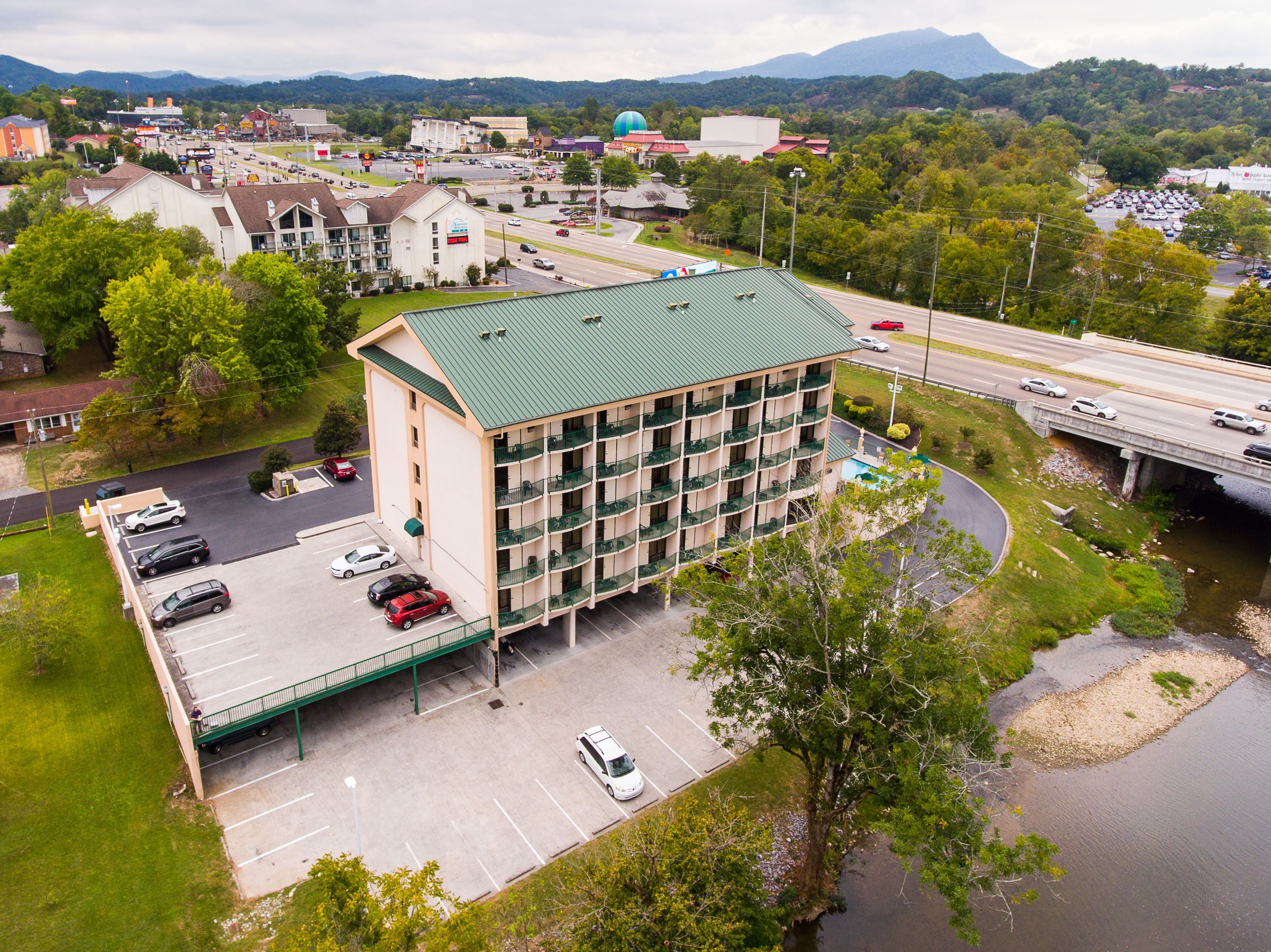A multi-story hotel with a green roof, a parking lot, and a river nearby.