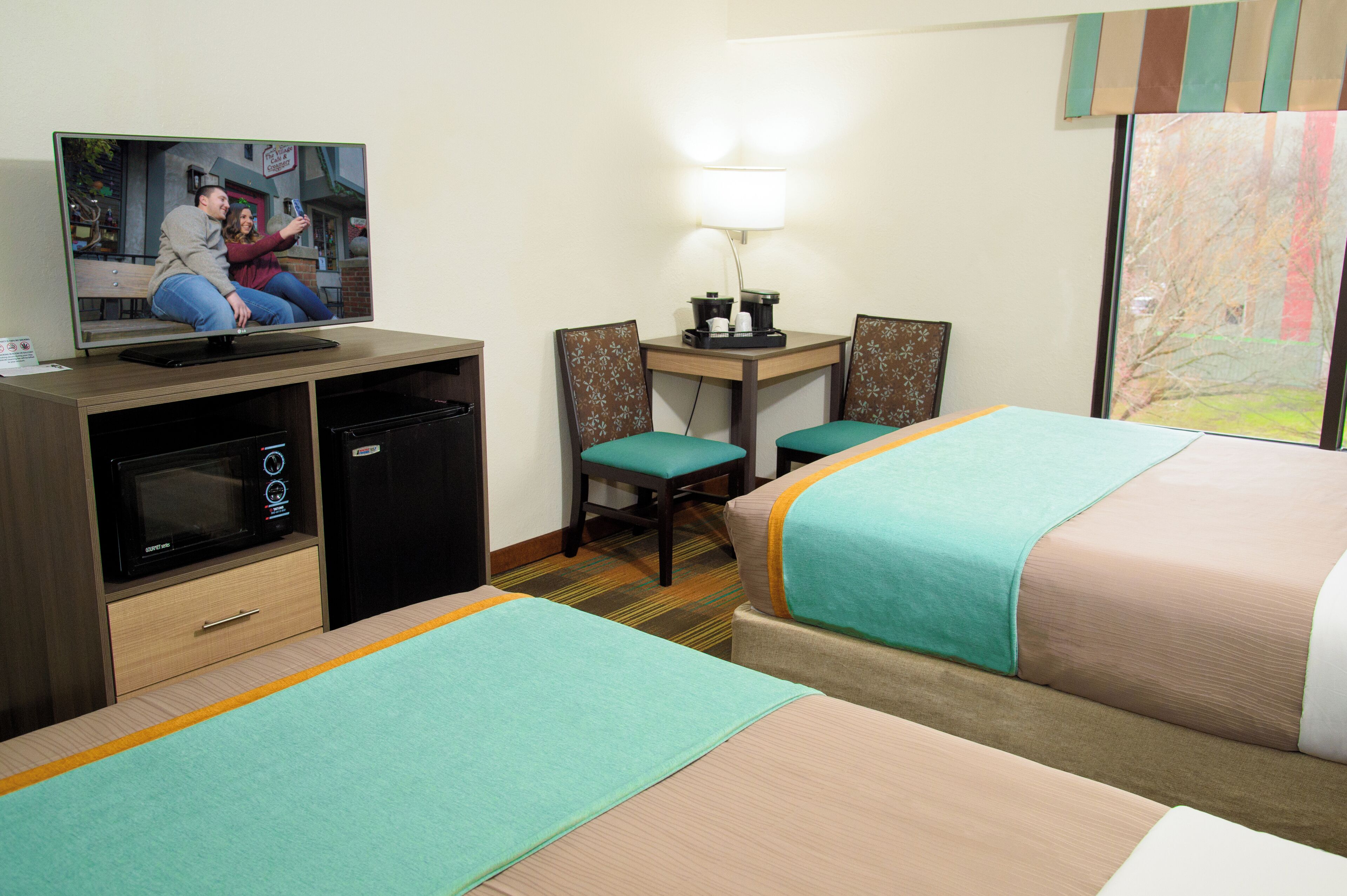 A hotel room with two beds, a desk, a television, a microwave, and a small refrigerator.