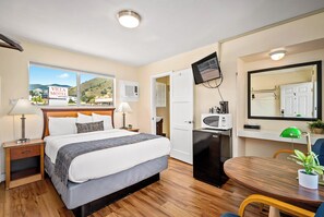 A hotel room with a bed, bedside tables, a desk with a chair, a TV, a microwave, and a view of the outside.