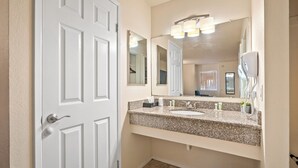 A bathroom with a white door, a granite countertop, a sink, a mirror, and a hairdryer. - Sunbeam Motel (San Luis Obispo)