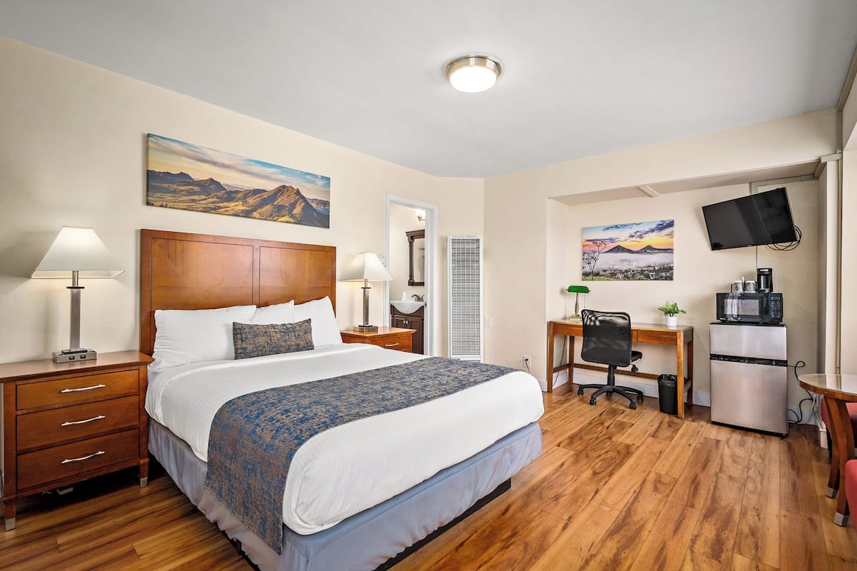 Une chambre d’hôtel équipée d’un lit, de tables de chevet, d’un bureau, d’une chaise, d’une télévision et d’une kitchenette.