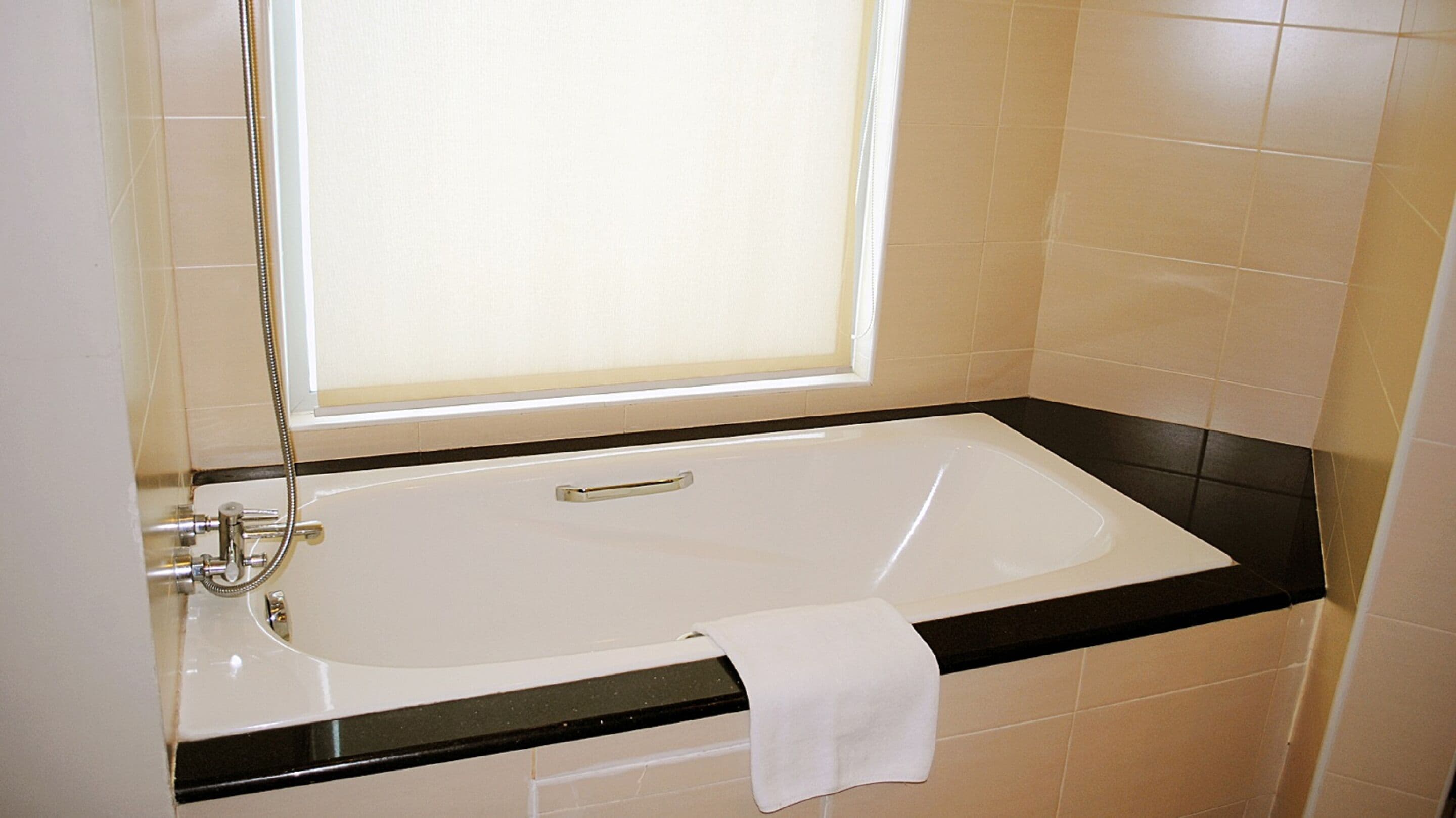 A modern bathroom with a white bathtub, black countertop, and beige tiles.
