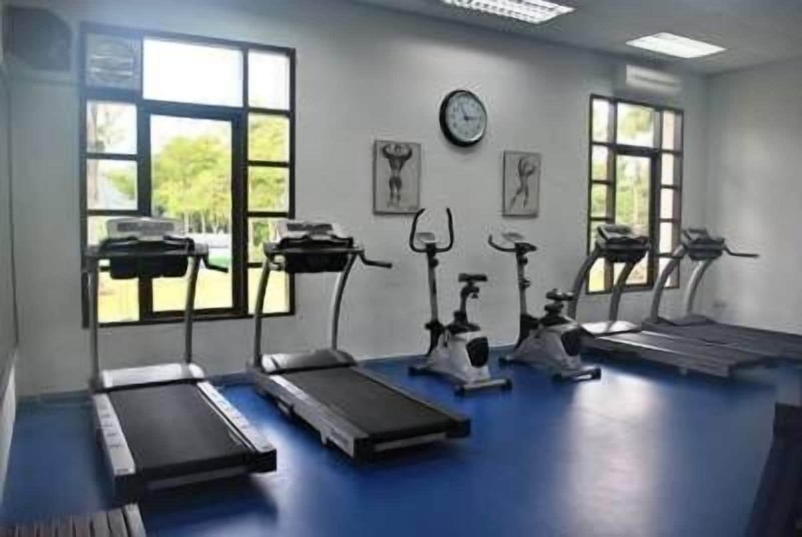 Un gimnasio con cintas de correr, bicicletas estáticas y un reloj de pared.